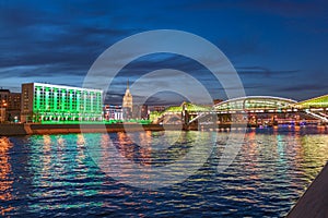 View of the colorful Bogdan Khmelnitsky bridge illuminated at night reflecting in the Moskva river. Moscow Kiyevsky railway