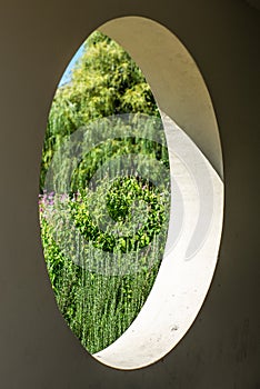 A view on a colorful garden in summer through a round hole in a concrete wall