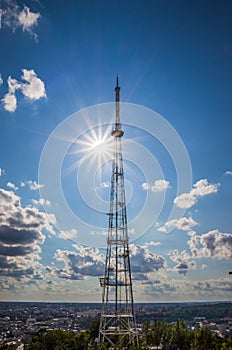 View of communication towers with blue sky, sun, mountain and cityscape background. Top view of the radio tower in the city