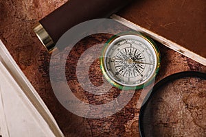 View of compass near copy book and magnifying glass on old world map