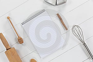 View of a composition with a notebook with cookie cutters, whisker and rolling pin on a white wooden