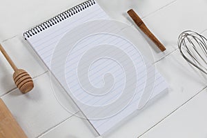 View of a composition with a notebook with wooden spoon and whisker on white wooden surface