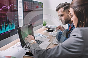 View of computer systems analysts using charts on computer monitors while working in office