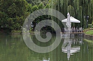 View of a cosy relaxation area under awnings with tables and chairs on the shores after rain of Lake Ariana, Borisova Gradina Park