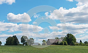 View of a country house with green grass in the foreground against a blue sky with white clouds in the background