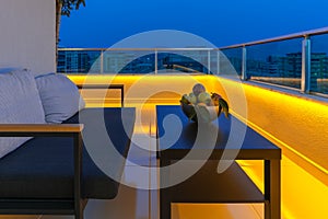 View of a cozy outdoor terrace with an armchair and a coffee table, LED lighting in the evening