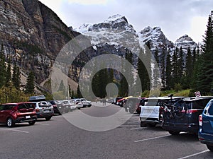 View of crowded parking lot of Moraine Lake, Banff National Park in the Canadian Rocky Mountains on cloudy day with Mount Bowlen.