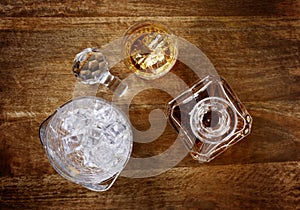 View of a crystal glass and decanter full of golden whisky, and ice bucket, shot from above on a dark wood