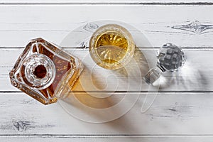 View of a crystal glass and decanter full of golden whisky, shot from above on a distressed white wooden background with copy