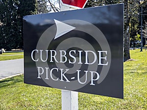 View of a curbside pickup sign in the grass outside a large business property during coronavirus