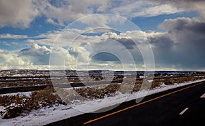 View of a curving road covered in snow way road during winter time, snow mountains in the distance