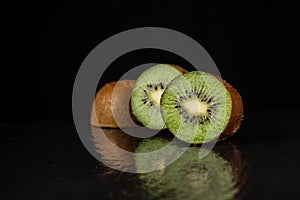 View of cut green kiwis on table with reflection, black background