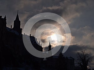 View of dark silhouette of Hohenzollern Castle in Sigmaringen, Swabian Alb, Germany with towers and bare trees in winter.