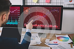 View of data analyst pointing on charts on computer monitor near laptop with blank screen on table photo