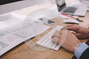 View of data analyst using computer keyboard near papers with graphs on table