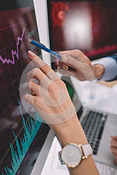 View of data analysts pointing on charts on computer monitors