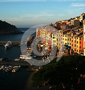 View at the dawn of Portovenere and harbor with moored boats, sea, colorful buildings, trees