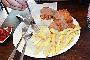 View of deep fried chicken and French fries on white plate with hand holding fork