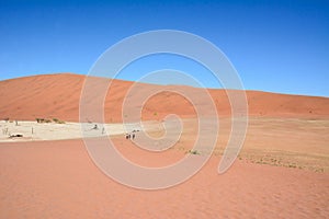 View of the desert dunes under the hot sun and blue sky. A few tourists are standing far ahead
