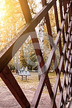 View through a diamond-shaped wooden hedge of young children playing in an park on a bench during fall foliage. kidnapping