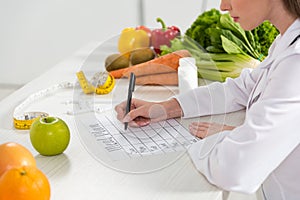 View of dietitian writing in meal plan at workplace