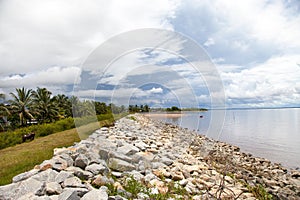 View of a dirt wall of boulders along the shore of the Atlantic ocean, Guyana on the background of blue sky