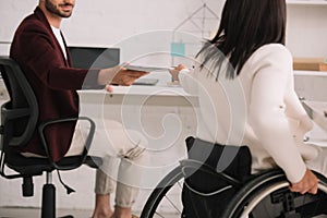 View of disabled businesswoman giving documents to colleague in office