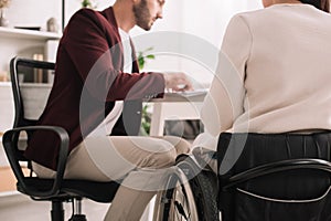 View of disabled businesswoman sitting at desk near colleague