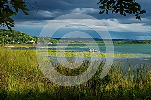 View on the dock with people along the lake shore with dark blue cloudscape, El Remate, Peten, Guatemala