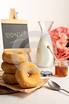 View of donuts on brown paper and white table with spoon, honey, milk bottle and blackboard, selective focus