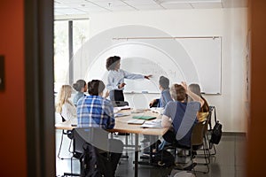 View Through Doorway Of High School Tutor At Whiteboard Teaching Maths Class