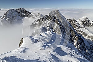 Pohľad na dramatické, skalnaté, zasnežené štíty pohorí s hmlou a oblakmi, Lomnický štít, Vysoké Tatry, Slovensko, Európske Alpy.