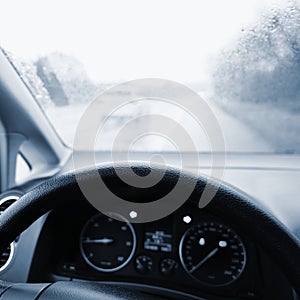 View from the driver - car interior with steering wheel and dashboard. Winter bad rainy weather and dangerous driving on the road