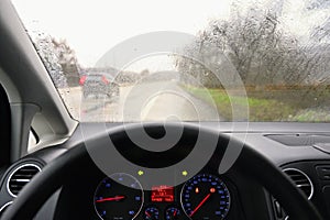 View from the driver - car interior with steering wheel and dashboard. Winter bad rainy weather and dangerous driving on the road