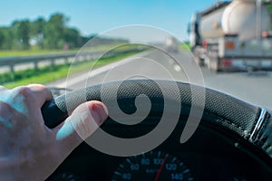 View driver hand on the wheel of a car that is driving along the highway