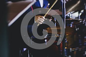 View of drum set kit on a stage during jazz rock show performance, with band performing in the background, drummer point of view