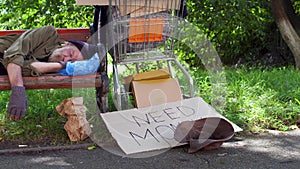 View of drunk homeless man sleeping at day time on the bench in the street.