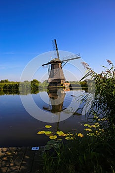 View on dutch water canal with reflection of one old windmill against deep blue cloudless summer sky in rural countryside -