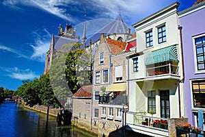 View on dutch water canal, waterfront residential houses with balconies and gothic church background, blue summer sky - Dordrecht