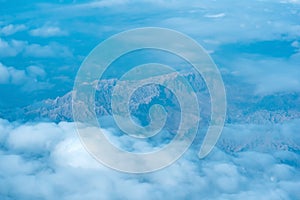 View of the earth below while flying above the clouds, mountainous terrain through atmospheric haze, view from above