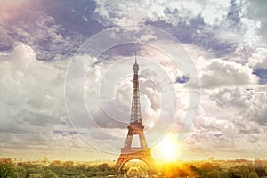 View on Eiffel tower through green summer trees with sunset rays. Beautiful Romantic background. Eiffel Tower from Champ