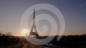 View of the Eiffel Tower from the Trocadero Gardens at dawn. The sun rises from the horizon.