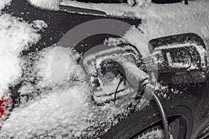 View of electric car with connected charging cable on frosty winter background.