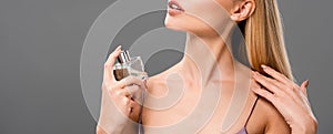 View of elegant blonde woman in satin violet dress spraying perfume with closed eyes isolated on grey