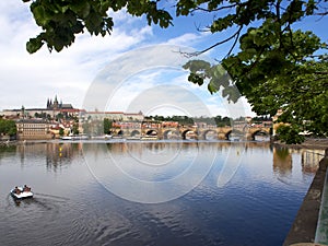 View of embankment of Vltava river in Prague with bridge, boat and blue sky