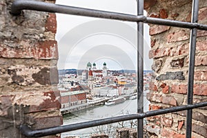 View through an embrasure in the castle wall of the fortress Feste Oberhaus near the three rivers city Passau with view on the cit