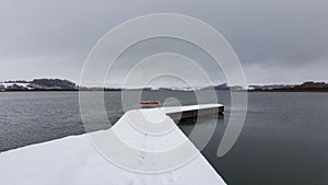 View of an empty bench in a wooden deck in the lake during winter