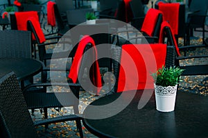 View of empty terrace of open air cafe with black tables and chairs with red blankets.