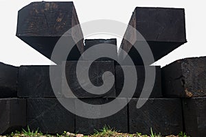 View of end parts of stacked rows of black tarred old rectangular railway sleepers lying on ground with grass, look of perspective