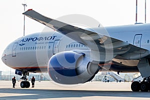 View on engine and cockpit of passenger jet aircraft Boeing 777-300ER of Aeroflot Airlines. Two workers check plane`s chassis.